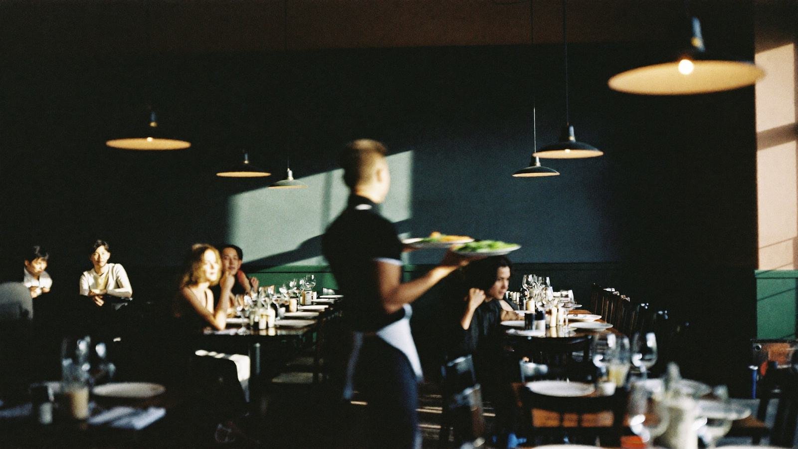 Une salle de restaurant en plein service, vue depuis le passe.