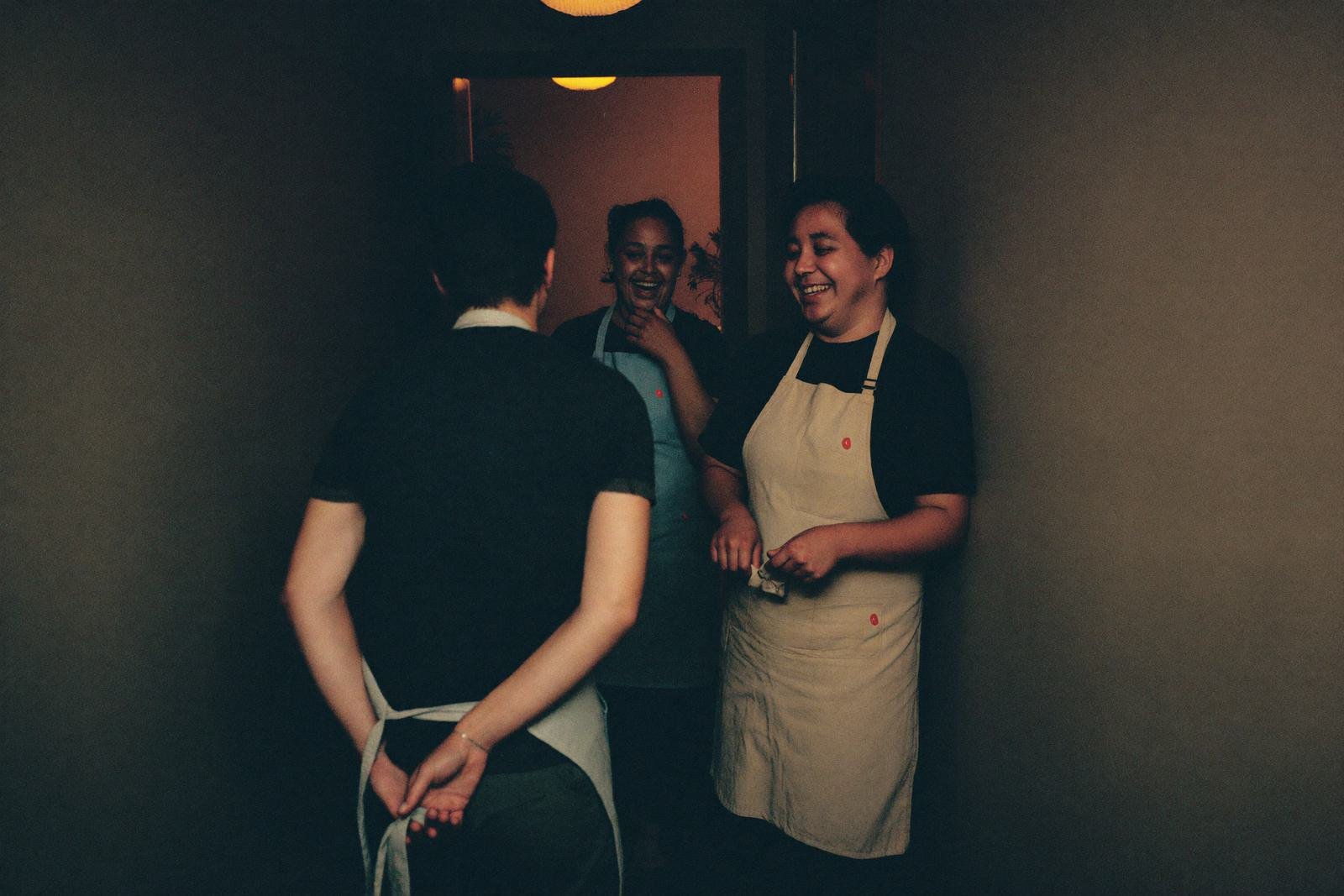 Trois membres du personnel en tablier discutent dans un couloir de service avant l'ouverture.