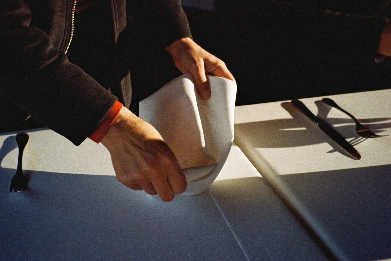 Des mains dressent une table et plient une serviette en lin.