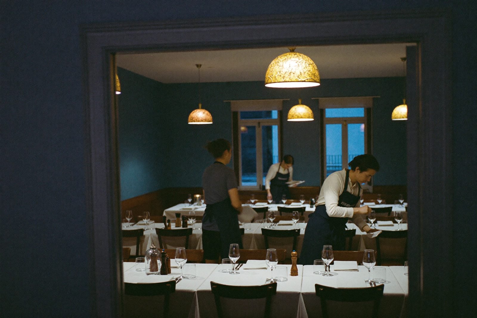 Trois membres de l'équipe préparent une salle de restaurant, chacun à une tâche différente, avant l'ouverture.