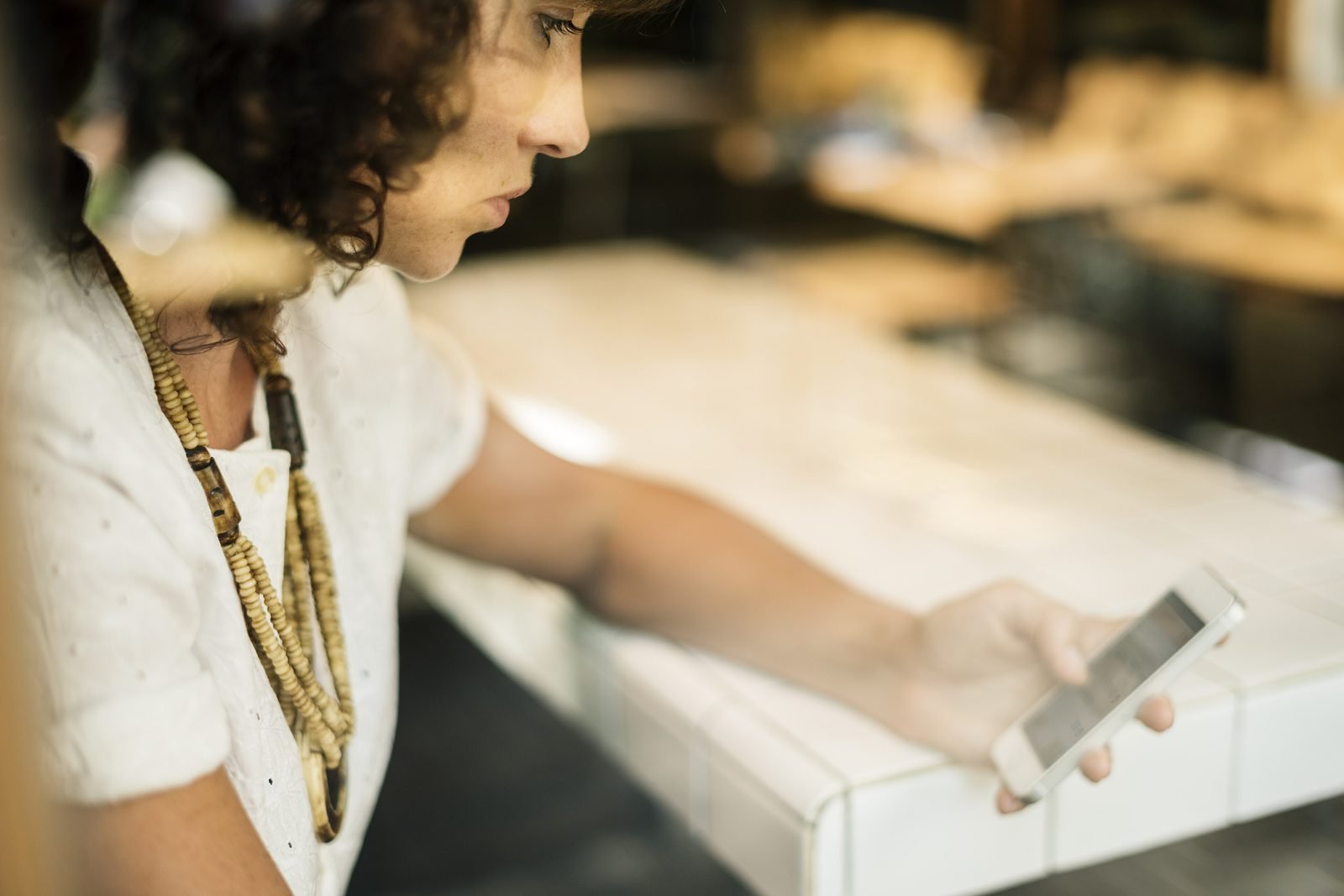 Une jeune femme consulte son téléphone, accoudée au comptoir d'une salle en fin de service.